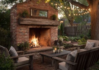 Outdoor fireplace in a country backyard featuring a classic red brick structure, rustic reclaimed wood mantel, bluestone hearth, warm string lights, and a cozy atmosphere, perfect for gatherings and late-night conversations.