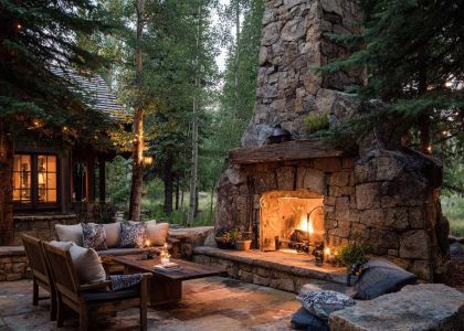 "Rustic outdoor fireplace made of large rough-hewn stones and a reclaimed wood mantel, surrounded by a flagstone patio in a serene forest clearing, creating a cozy gathering spot illuminated by a warm glow, ideal for relaxing under the stars."