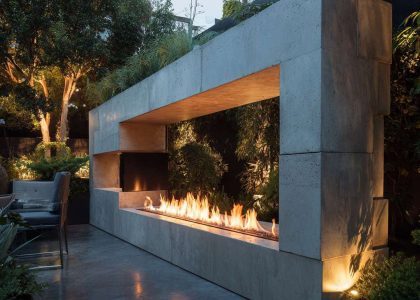 Sleek modern minimalist outdoor fireplace made of light gray concrete on polished patio with linear flame, surrounded by lush greenery and subtle integrated lighting, creating a tranquil retreat for relaxing moments under the stars.